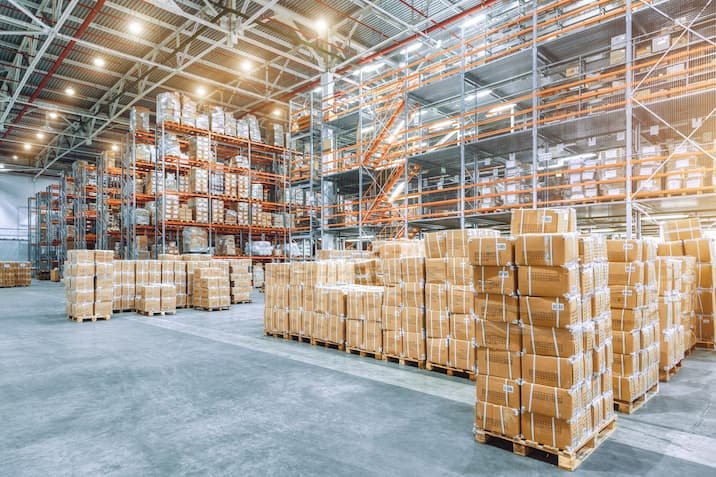 Large industrial warehouse with high racks. In the foreground are a lot of cardboard boxes.