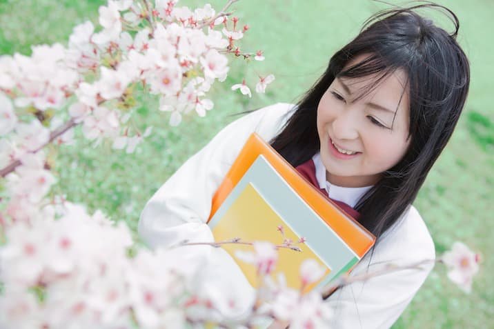 ノートを持って桜の木の下に立つ高校生